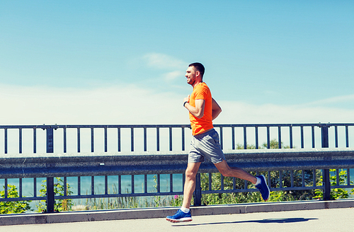 fitness, sport, people, technology and healthy lifestyle concept - smiling young man with heart rate watch running at summer seaside