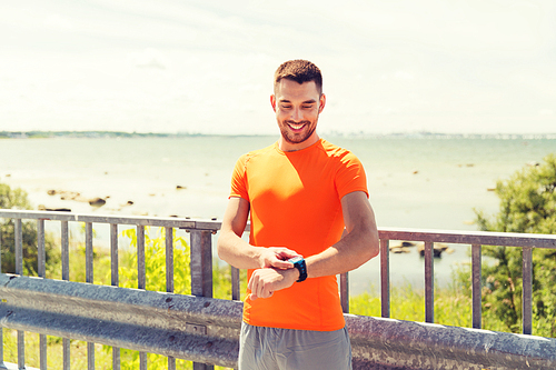 fitness, sport, people, technology and healthy lifestyle concept - smiling young man with smart wristwatch at summer seaside