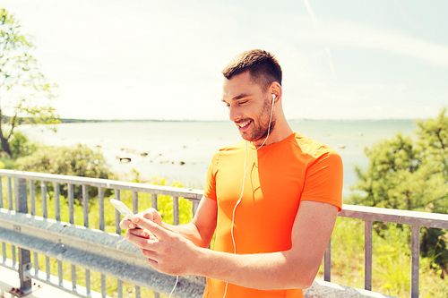 fitness, sport, people, technology and healthy lifestyle concept - smiling young man with smartphone and earphones listening to music at summer seaside