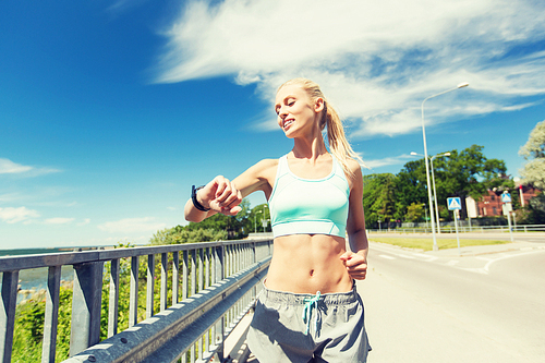 fitness, sport, people, technology and healthy lifestyle concept - smiling young woman with heart rate watch running outdoors