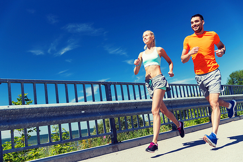 fitness, sport, friendship and healthy lifestyle concept - smiling couple running at summer seaside