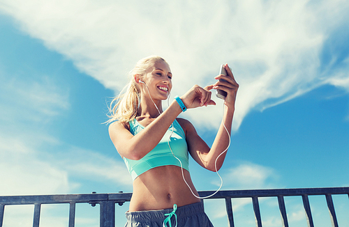 fitness, sport, people, technology and healthy lifestyle concept - smiling young woman with smartphone and earphones listening to music and exercising outdoors