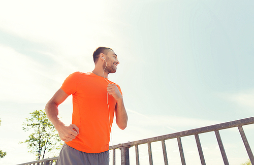 fitness, sport, people, technology and healthy lifestyle concept - happy man with earphones running outdoors