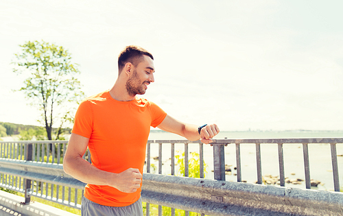 fitness, sport, people, technology and healthy lifestyle concept - smiling young man with smart wristwatch at summer seaside