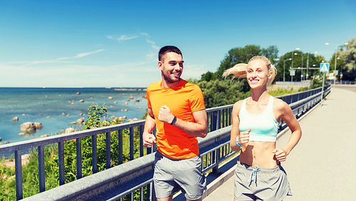 fitness, sport, friendship and healthy lifestyle concept - smiling couple with heart-rate watch running at summer seaside