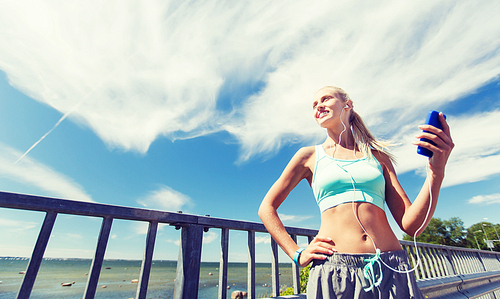 fitness, sport, people, technology and healthy lifestyle concept - smiling young woman with smartphone and earphones listening to music and exercising outdoors