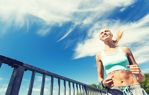 fitness, sport, people, technology and healthy lifestyle concept - smiling young woman with heart rate watch running outdoors