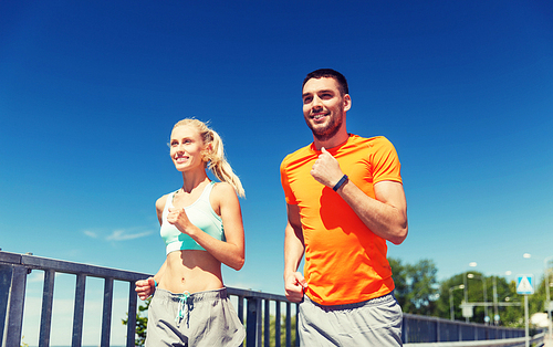 fitness, sport, friendship and healthy lifestyle concept - smiling couple with heart-rate watch running at summer seaside