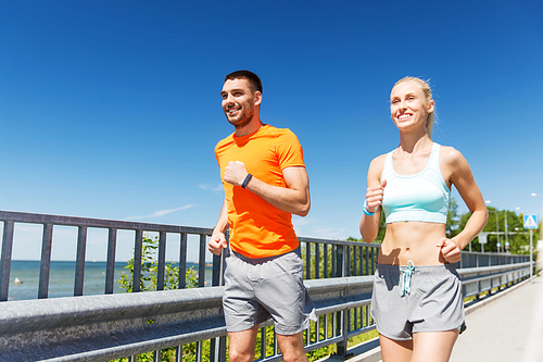 fitness, sport, friendship and healthy lifestyle concept - smiling couple with heart-rate watch running at summer seaside