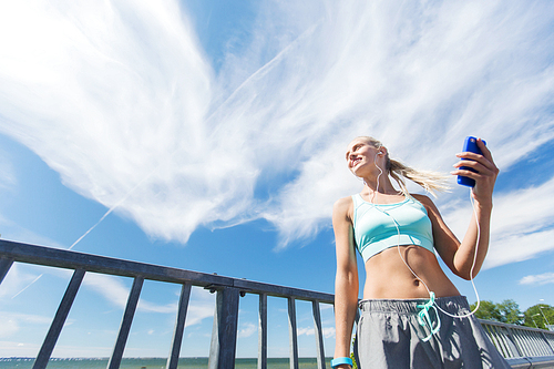 fitness, sport, people, technology and healthy lifestyle concept - smiling young woman with smartphone and earphones listening to music and exercising outdoors