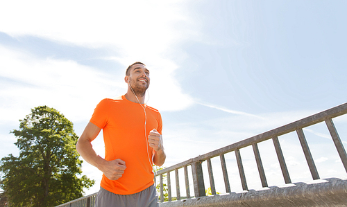 fitness, sport, people, technology and healthy lifestyle concept - happy man with earphones running outdoors