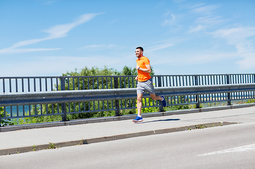 fitness, sport, people, technology and healthy lifestyle concept - smiling young man with heart rate watch running at summer seaside