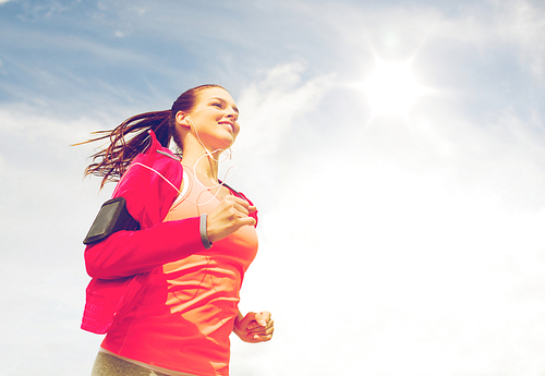 fitness, sport and lifestyle concept - smiling young woman with earphones running outdoors