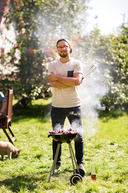 leisure, food, people and holidays concept - happy young man cooking meat on barbecue grill at outdoor summer party