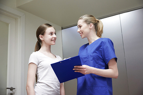 medicine, health care and people concept - smiling female doctor or nurse with clipboard and young girl meeting at hospital
