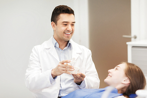 people, medicine, stomatology and health care concept - happy male dentist showing jaw layout to patient girl at dental clinic office