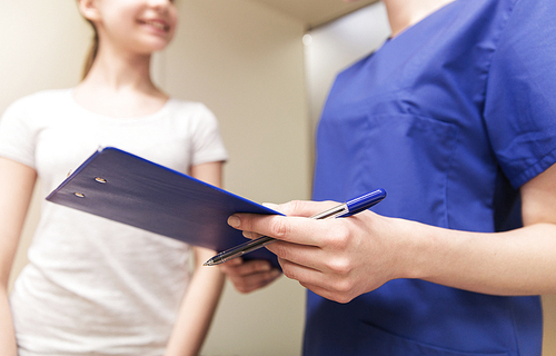 medicine, health care and people concept - close up of female doctor or nurse holding clipboard with pen and talking to girl at hospital