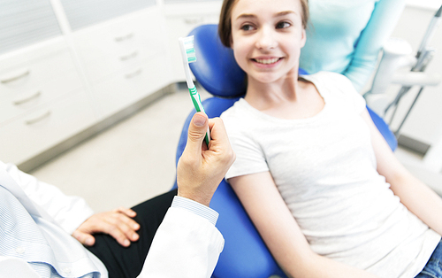 people, medicine, stomatology and health care concept -close up of dentist hand holding toothbrush and patient girl at dental clinic office