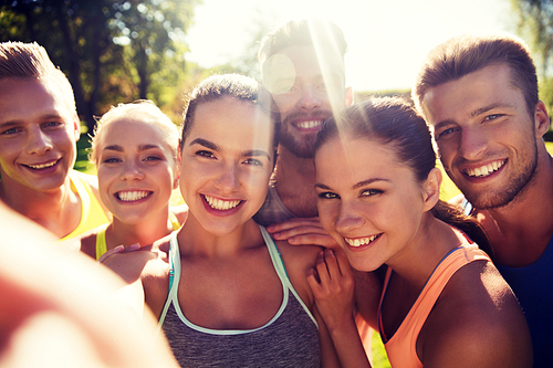 fitness, sport, friendship, technology and healthy lifestyle concept - group of happy teenage friends taking selfie with smartphone outdoors