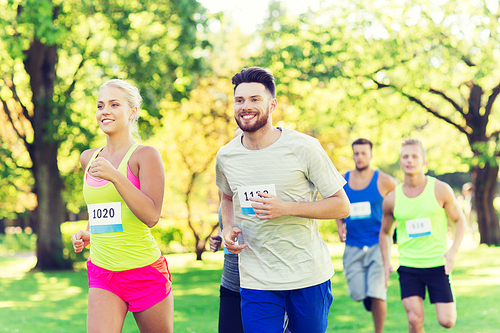 fitness, sport, friendship, race and healthy lifestyle concept - group of happy teenage friends or sportsmen running marathon with badge numbers outdoors