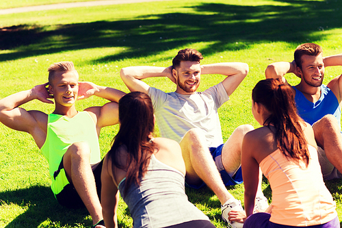 fitness, sport, friendship and healthy lifestyle concept - group of happy teenage friends or sportsmen exercising and doing sit-ups at boot camp