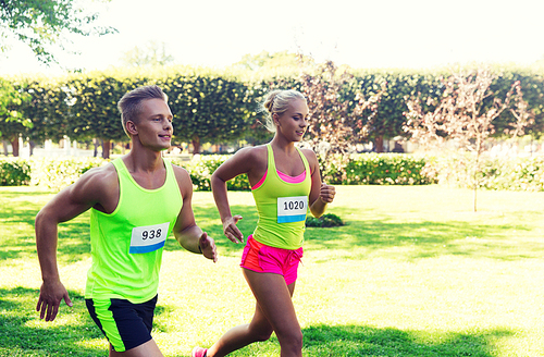 fitness, sport, friendship, race and healthy lifestyle concept - happy teenage friends or sportsmen couple running marathon with badge numbers outdoors