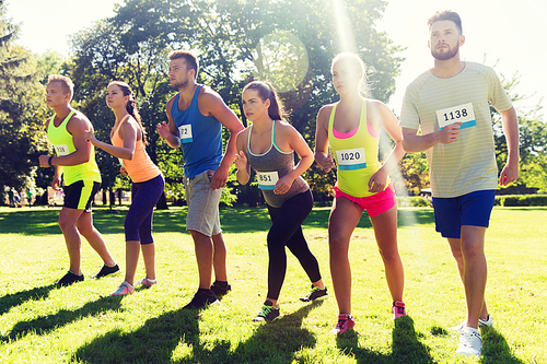 fitness, sport, race and healthy lifestyle concept - group of teenage friends or sportsmen with badge numbers on start of running marathon outdoors