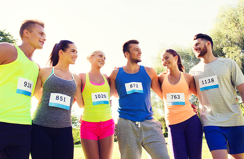 fitness, sport, marathon, friendship and healthy lifestyle concept - group of happy teenage friends or sportsmen couple with racing badge numbers outdoors