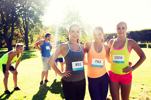 fitness, sport, friendship, marathon and healthy lifestyle concept - happy young sporty women with racing badge numbers outdoors