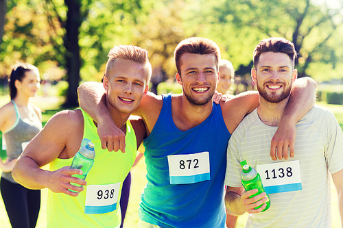 fitness, sport, friendship, marathon and healthy lifestyle concept - group of happy teenage friends or sportsmen with racing badge numbers and water bottles outdoors