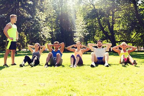 fitness, sport, friendship and healthy lifestyle concept - group of happy teenage friends or sportsmen exercising and doing sit-ups at boot camp