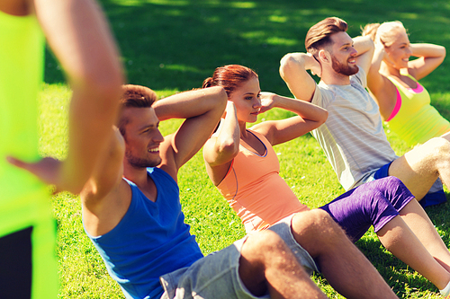 fitness, sport, friendship and healthy lifestyle concept - group of happy teenage friends or sportsmen exercising and doing sit-ups at boot camp