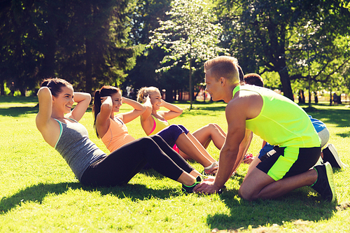 fitness, sport, friendship and healthy lifestyle concept - group of happy teenage friends or sportsmen exercising and doing sit-ups at boot camp