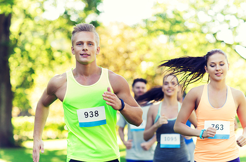 fitness, sport, friendship, race and healthy lifestyle concept - group of happy teenage friends or sportsmen running marathon with badge numbers outdoors