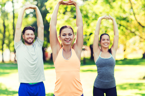 fitness, sport, friendship and healthy lifestyle concept - group of happy teenage friends or sportsmen exercising and stretching hands up at boot camp