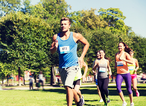 fitness, sport, race and healthy lifestyle concept - group of happy teenage friends or sportsmen running marathon with badge numbers outdoors