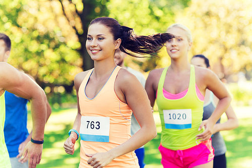 fitness, sport, friendship, race and healthy lifestyle concept - group of happy teenage friends or sportsmen running marathon with badge numbers outdoors