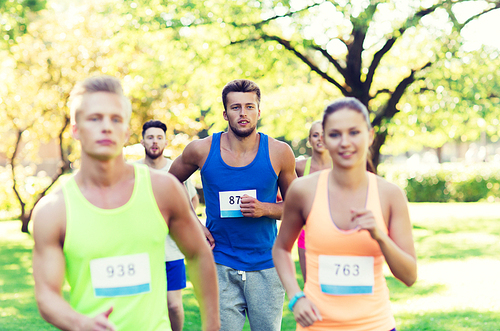 fitness, sport, friendship, race and healthy lifestyle concept - group of happy teenage friends or sportsmen running marathon with badge numbers outdoors