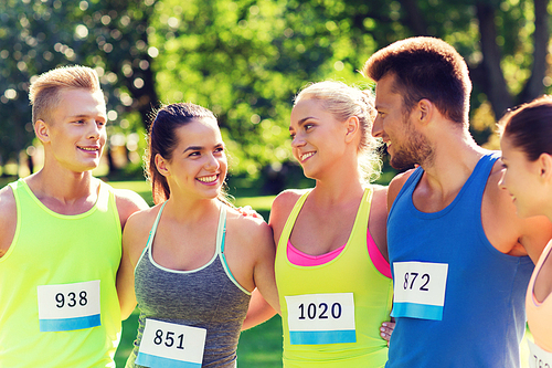 fitness, sport, marathon, friendship and healthy lifestyle concept - group of happy teenage friends or sportsmen couple with racing badge numbers outdoors