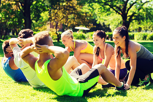 fitness, sport, friendship and healthy lifestyle concept - group of happy teenage friends or sportsmen exercising and doing sit-ups at boot camp