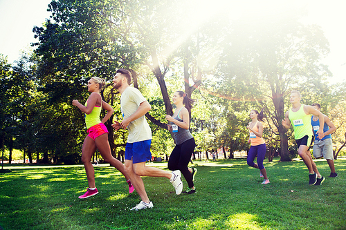 fitness, sport, friendship, race and healthy lifestyle concept - group of happy teenage friends or sportsmen running marathon with badge numbers outdoors