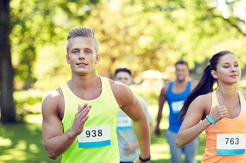 fitness, sport, friendship, race and healthy lifestyle concept - group of happy teenage friends or sportsmen running marathon with badge numbers outdoors