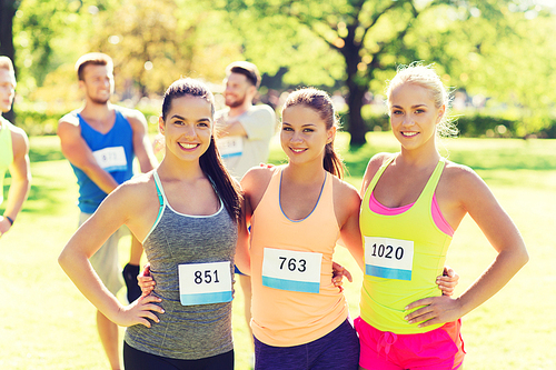 fitness, sport, friendship, marathon and healthy lifestyle concept - happy young sporty women with racing badge numbers outdoors