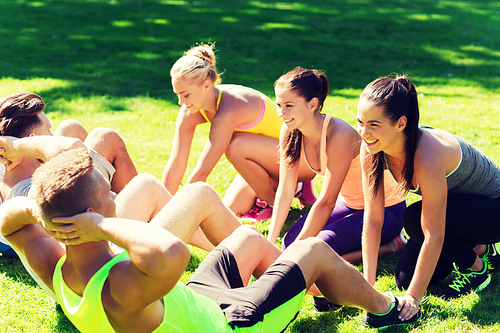 fitness, sport, friendship and healthy lifestyle concept - group of happy teenage friends or sportsmen exercising and doing sit-ups at boot camp