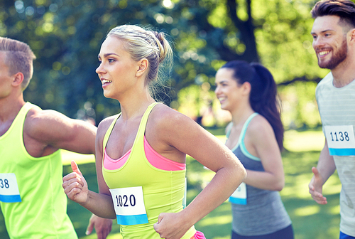 fitness, sport, friendship, race and healthy lifestyle concept - group of happy teenage friends or sportsmen running marathon with badge numbers outdoors