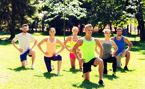 fitness, sport, friendship and healthy lifestyle concept - group of happy teenage friends or sportsmen exercising and stretching knee at boot camp