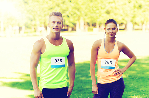 fitness, sport, friendship, marathon and healthy lifestyle concept - group of happy teenage friends or sportsmen couple with racing badge numbers outdoors