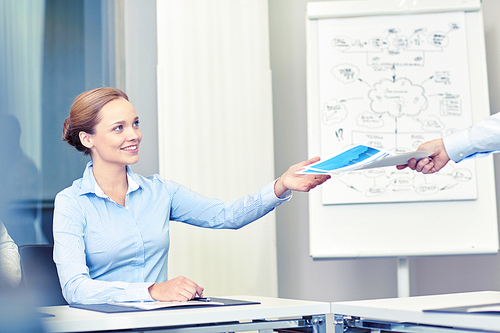 business and people concept - smiling businesswoman receiving papers from someone in office