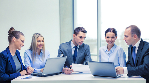 business, technology and office concept - smiling business team with laptop computers and documents having discussion in office