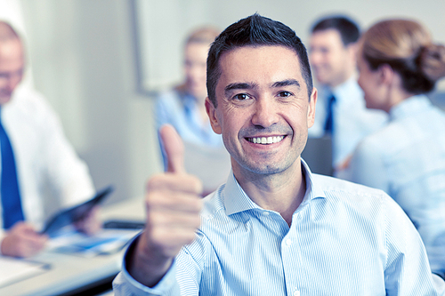 business, people, gesture and teamwork concept - smiling businessman showing thumbs up with group of businesspeople meeting in office